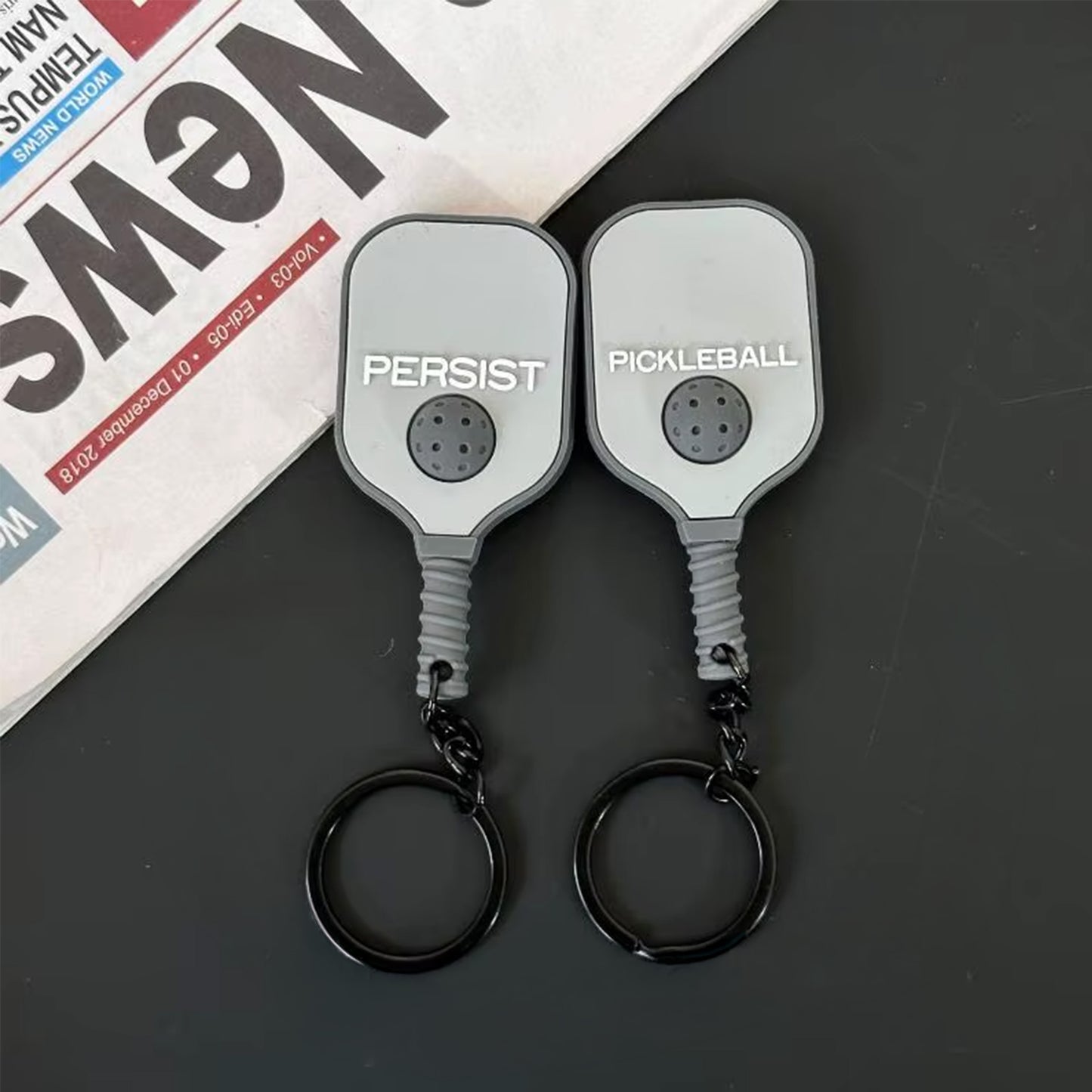 Porte-clés pickleball en silicone gris, montrant les deux faces du produit.