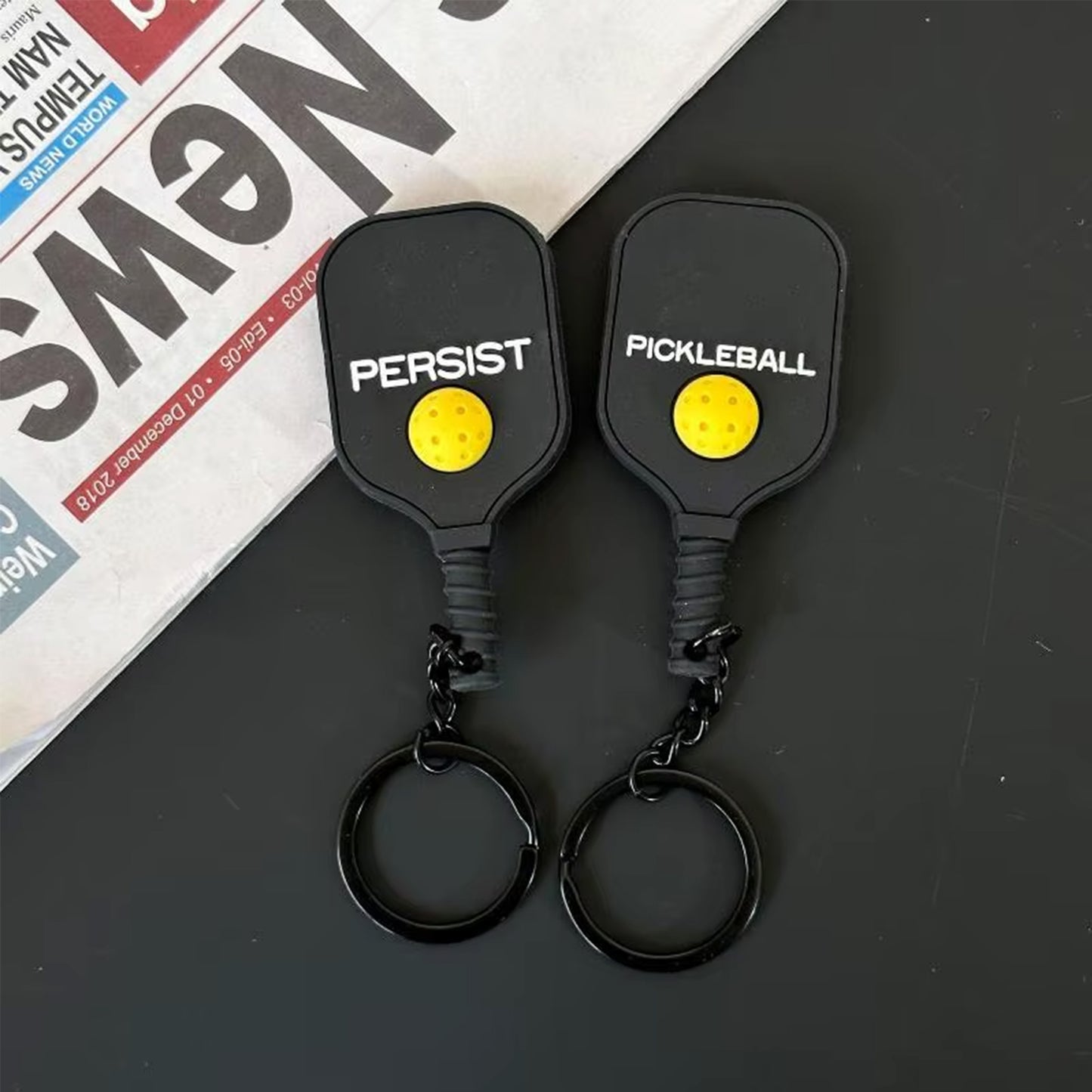 Mini porte-clés en forme de raquette noire avec sa petite balle jaune en relief au dos.