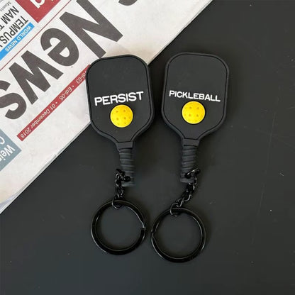 Mini porte-clés en forme de raquette noire avec sa petite balle jaune en relief au dos.