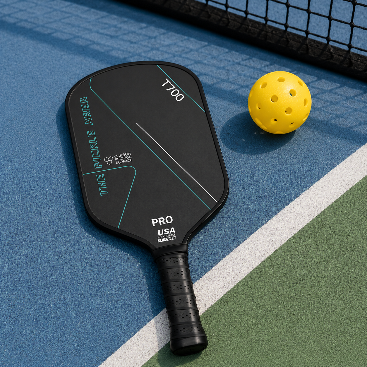 Modèle T700 Pro Area noir et cyan posé sur le revêtement bleu d'un terrain à côté d'une balle de pickleball jaune.
