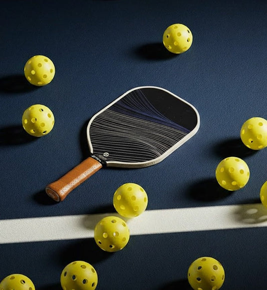 Raquette Wave de Smashline posée sur un terrain avec des balles de pickleball jaunes autour.