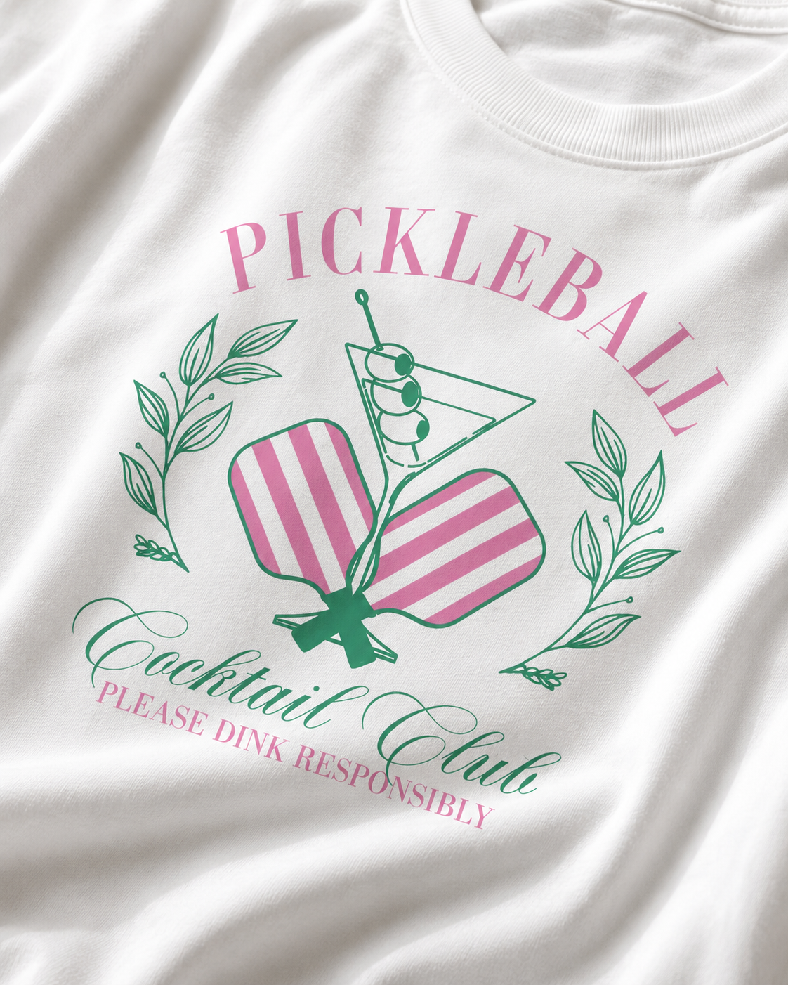 Gros plan sur l'illustration du t-shirt : deux raquettes à rayures roses, un verre à cocktail et l'inscription verte et rose.